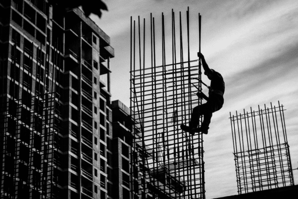 Construction worker climbing scaffolding amidst urban building structures in black and white.